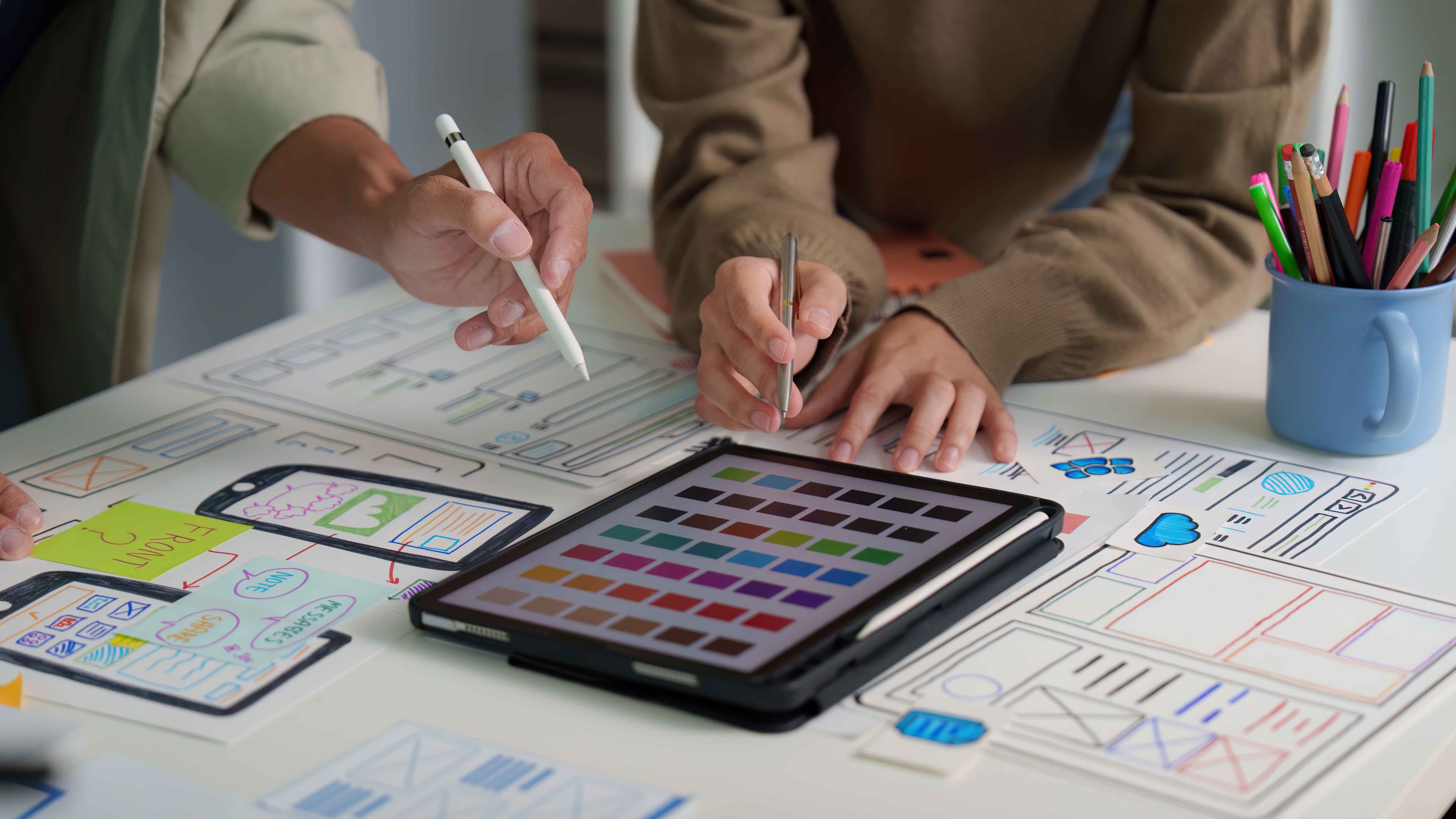 Two designers discussing UI/UX Design over a tablet with a colour palette 
