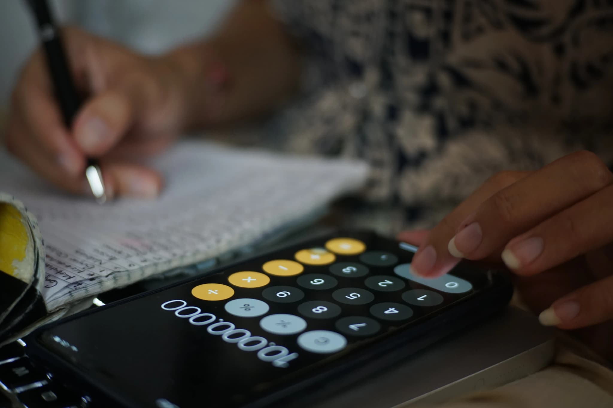 Woman using calculator on mobile with pen and paper to work our web design pricing